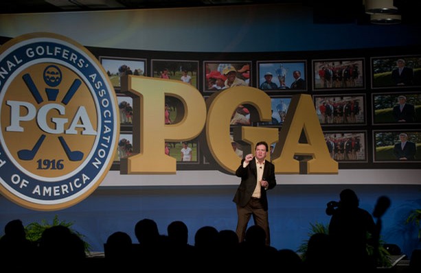 Jim Carroll onstage beneath the PGA of America emblem and giant PGA letters